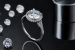 CARISSIE round moissanite halo engagement ring, lifestyle shot on black surface with scattered loose stones