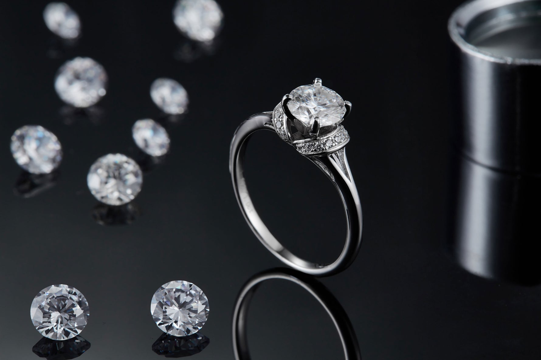 CARISSIE round moissanite solitaire ring, lifestyle shot on black surface with loose stones and studio lighting reflection