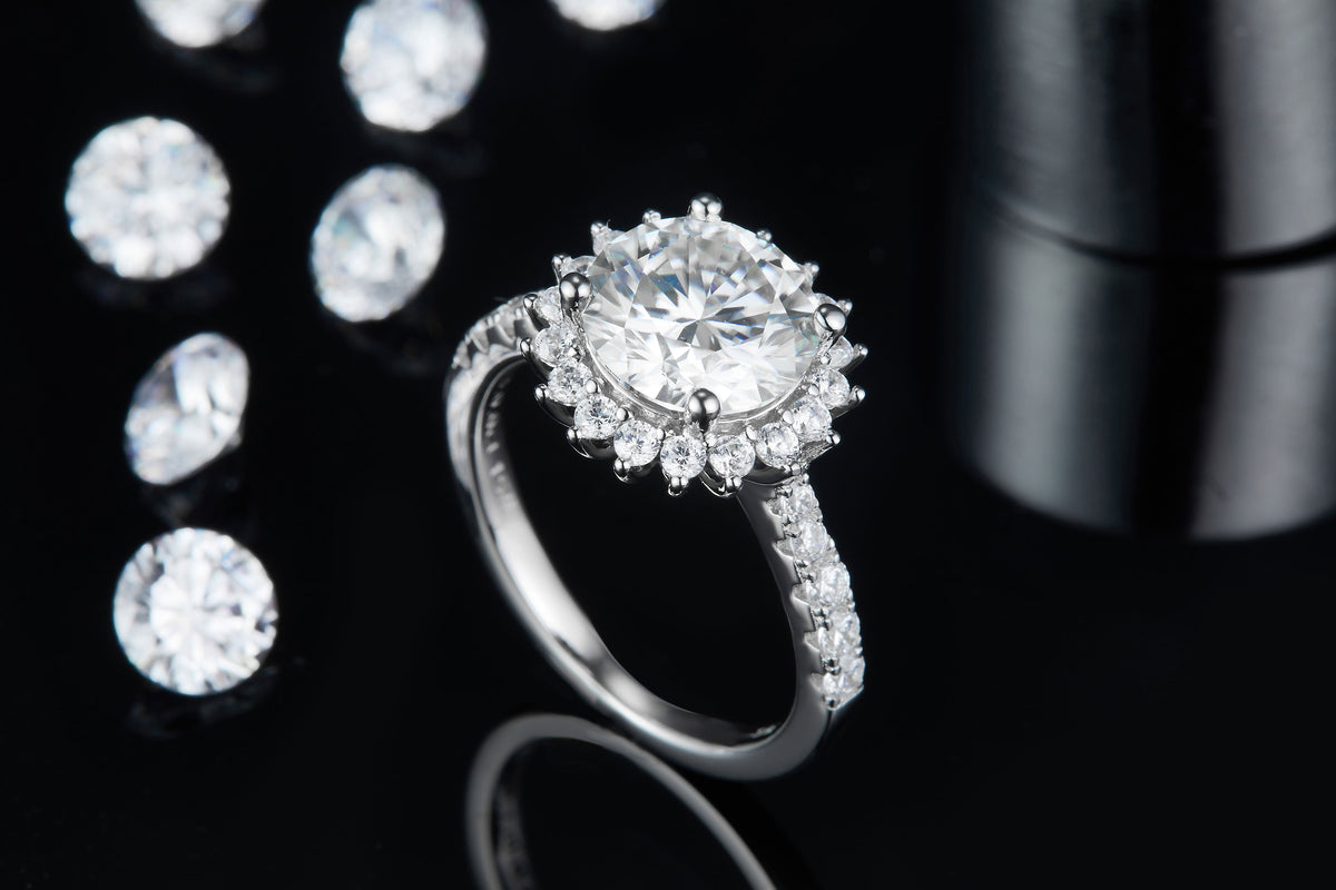 CARISSIE round moissanite halo engagement ring, lifestyle shot on black background with scattered loose stones for contrast