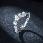 CARISSIE round moissanite solitaire band, lifestyle shot against blue bokeh background showing the tapered shank design