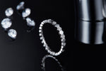 CARISSIE round moissanite eternity band, side profile standing upright against dark backdrop with scattered gems