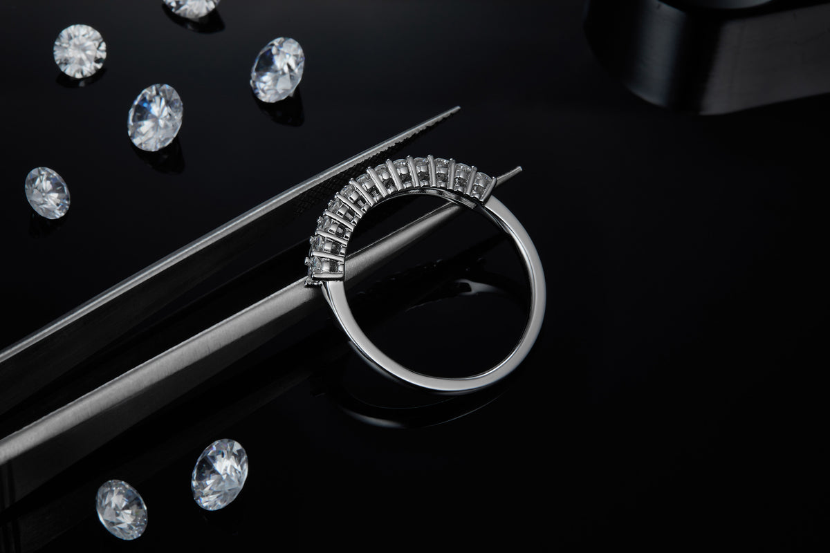 CARISSIE round moissanite eternity band, close-up held by tweezers revealing detailed craftsmanship against dark background