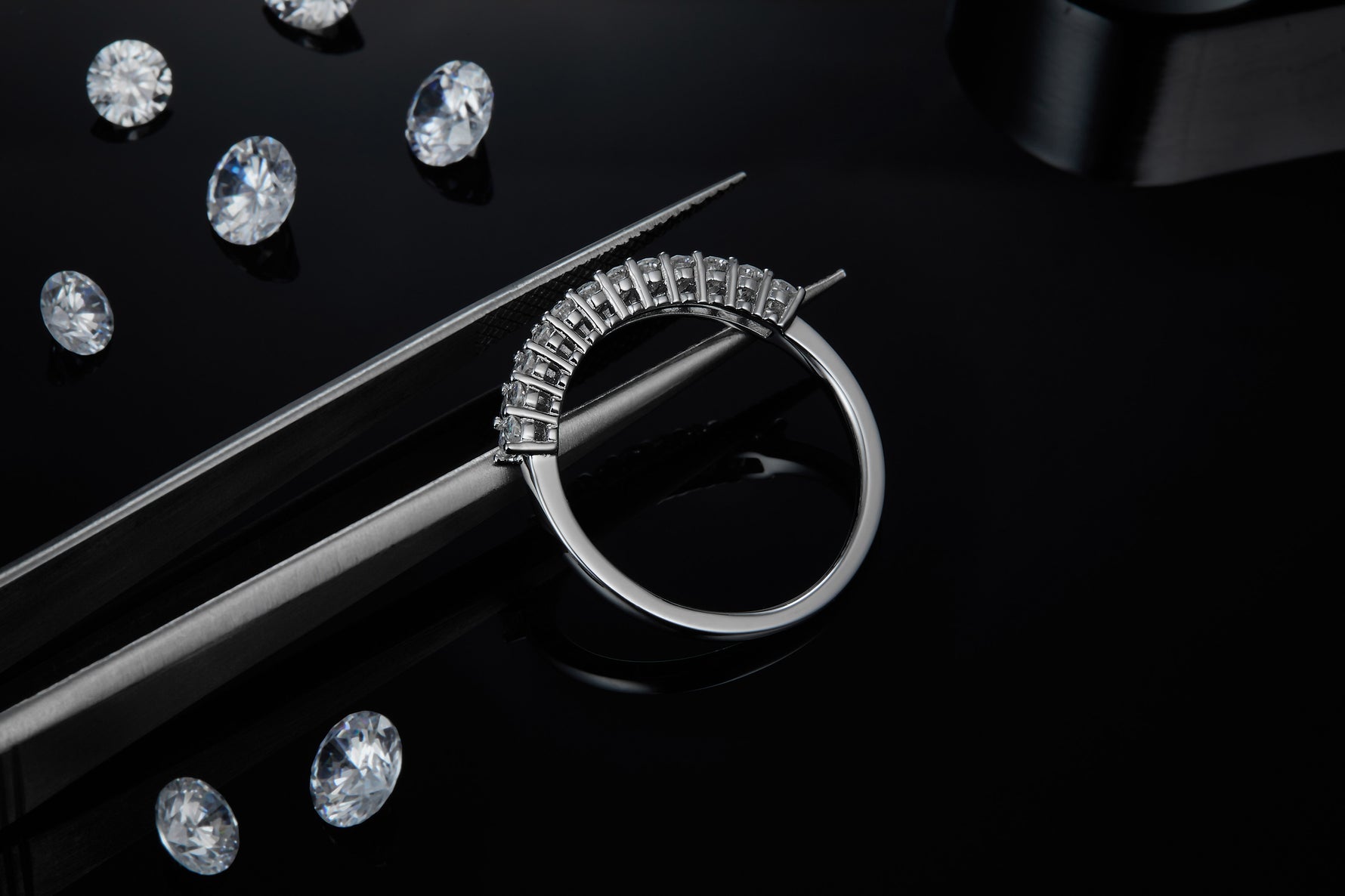 CARISSIE round moissanite eternity band, close-up held by tweezers revealing detailed craftsmanship against dark background