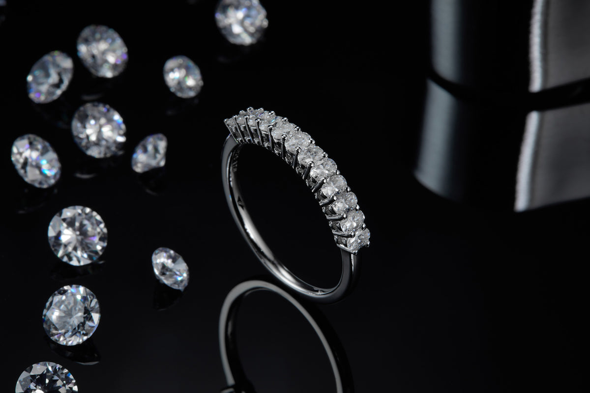 CARISSIE round moissanite eternity band, artistic shot standing on edge surrounded by loose gemstones to emphasize sparkle