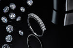 CARISSIE round moissanite eternity band, artistic shot standing on edge surrounded by loose gemstones to emphasize sparkle