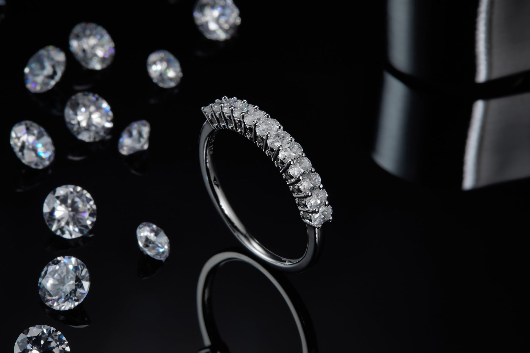 CARISSIE round moissanite eternity band, artistic shot standing on edge surrounded by loose gemstones to emphasize sparkle