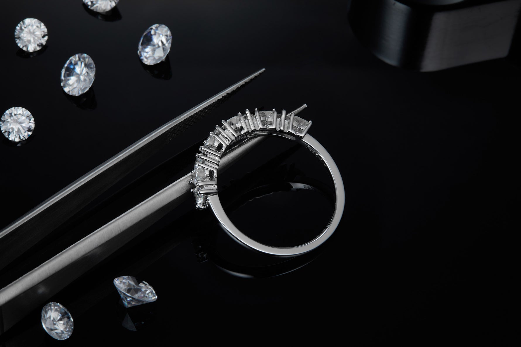 CARISSIE round moissanite eternity band, lifestyle shot on black reflective surface surrounded by loose gemstones