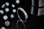 CARISSIE eternity band, lifestyle shot on black reflective surface with scattered round loose stones in background