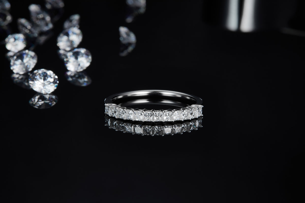 CARISSIE Princess Moissanite Eternity Band, horizontal side profile on a dark mirror base emphasizing the perfect symmetry of the geometric stones.