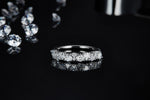CARISSIE round moissanite eternity band, low-angle shot on a dark background emphasizing the sparkle and reflection.