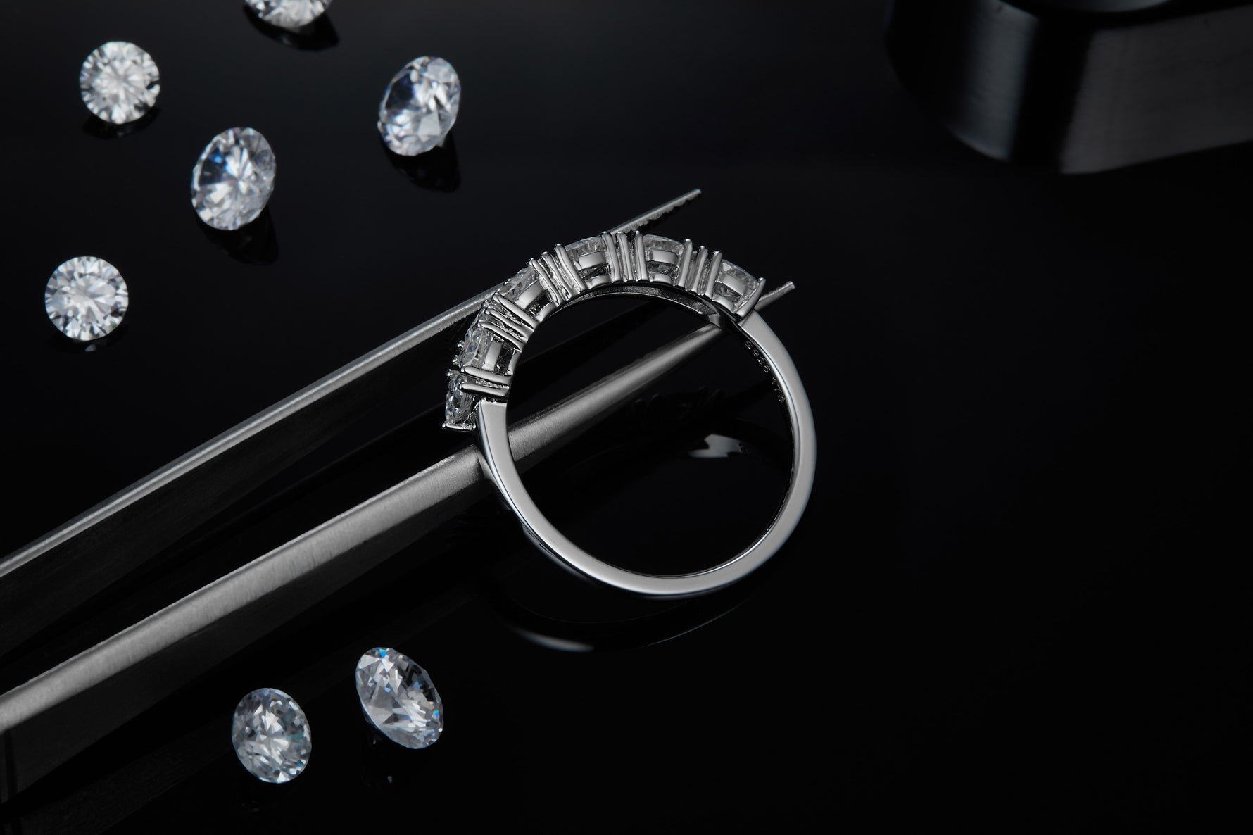 CARISSIE round moissanite eternity band, side profile held by tweezers revealing the open gallery and prong structure.
