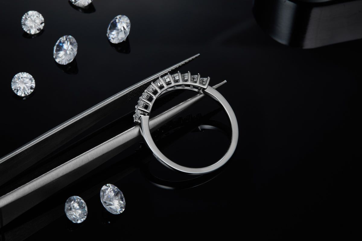 CARISSIE round moissanite solitaire ring, close-up held by tweezers showcasing the detailed craftsmanship of the prong settings against a dark backdrop