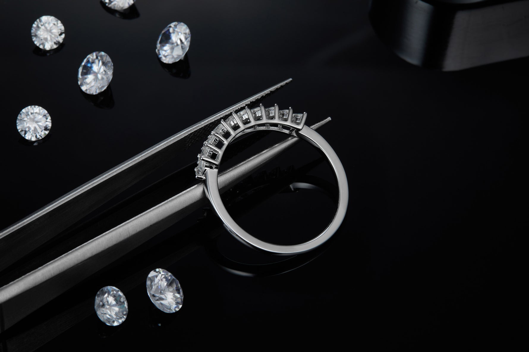 CARISSIE round moissanite solitaire ring, close-up held by tweezers showcasing the detailed craftsmanship of the prong settings against a dark backdrop