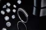 CARISSIE round moissanite solitaire ring, lifestyle shot on a black reflective background with loose gemstones emphasizing sparkle and contrast