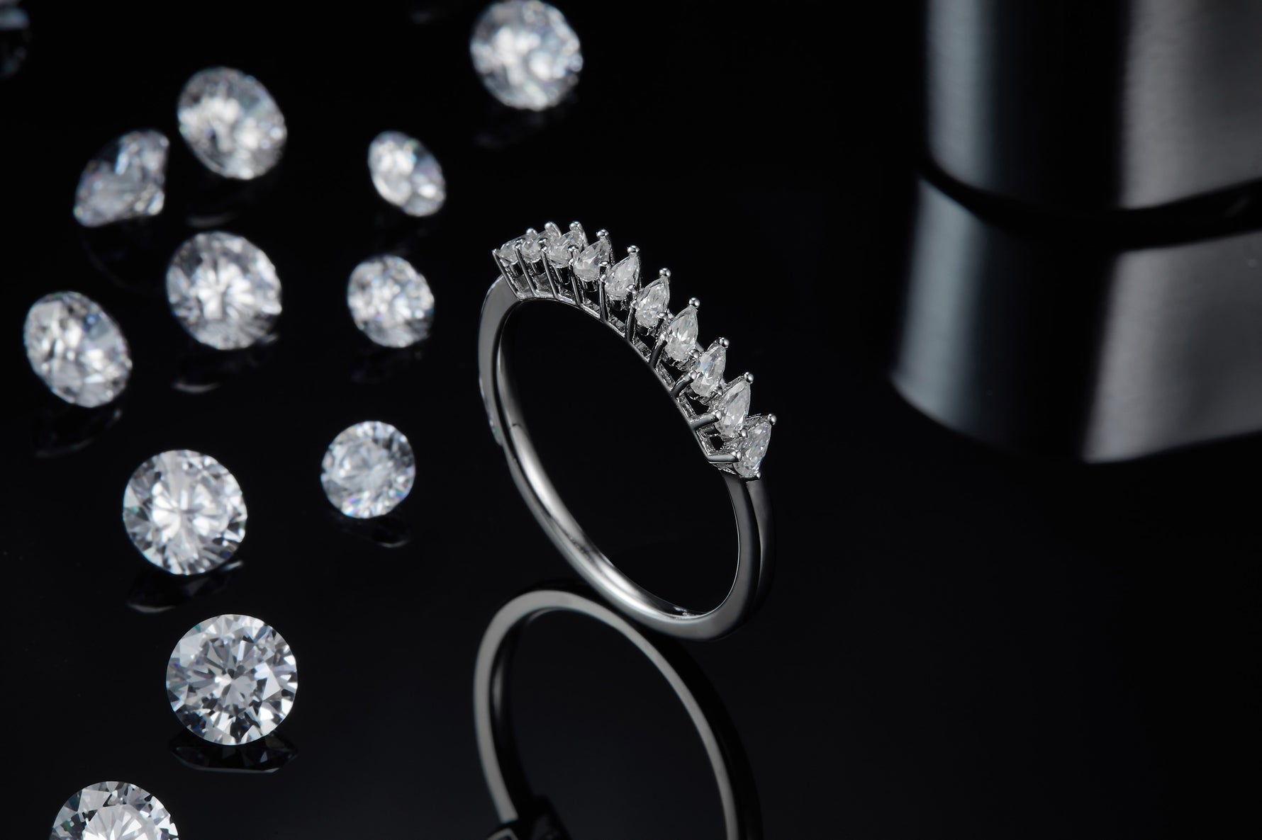 CARISSIE round moissanite solitaire ring, lifestyle shot on a black reflective background with loose gemstones emphasizing sparkle and contrast