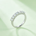 CARISSIE oval moissanite eternity band, lifestyle shot on soft green background with natural light casting gentle shadows across the sparkling stones
