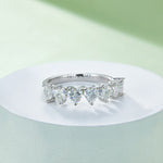 CARISSIE heart moissanite eternity band, resting on a white pedestal with bright light reflecting off the facets of the heart stones.