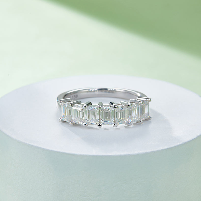 CARISSIE emerald cut moissanite ring, angled shot on white pedestal highlighting the sparkle of step-cut stones
