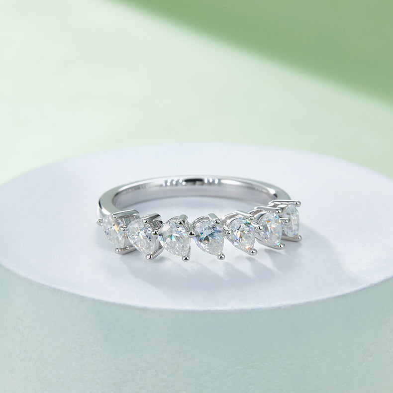 CARISSIE pear moissanite eternity band, displayed on a white pedestal showcasing the continuous curve of the seven-stone design