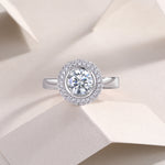 CARISSIE round moissanite halo engagement ring, lifestyle shot on textured paper showcasing brilliant sparkle in soft light