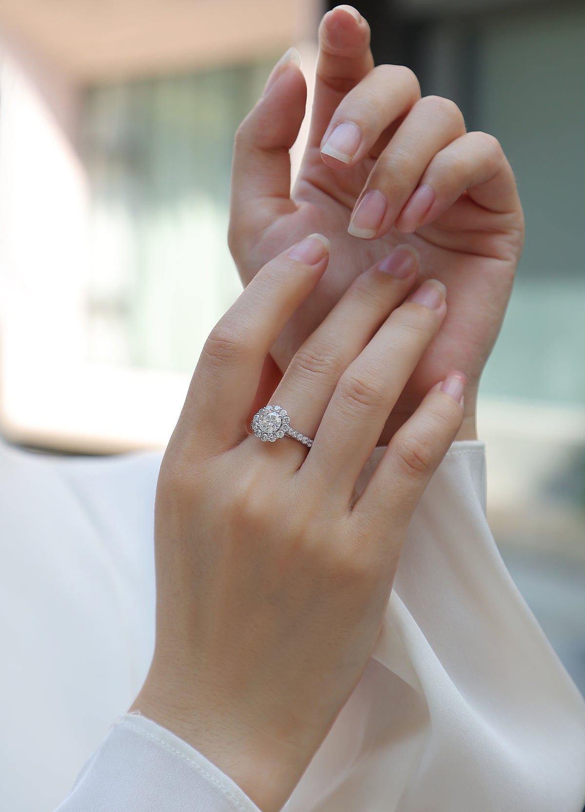CARISSIE round moissanite halo engagement ring on hand, showing elegant fit and pavé band against white fabric