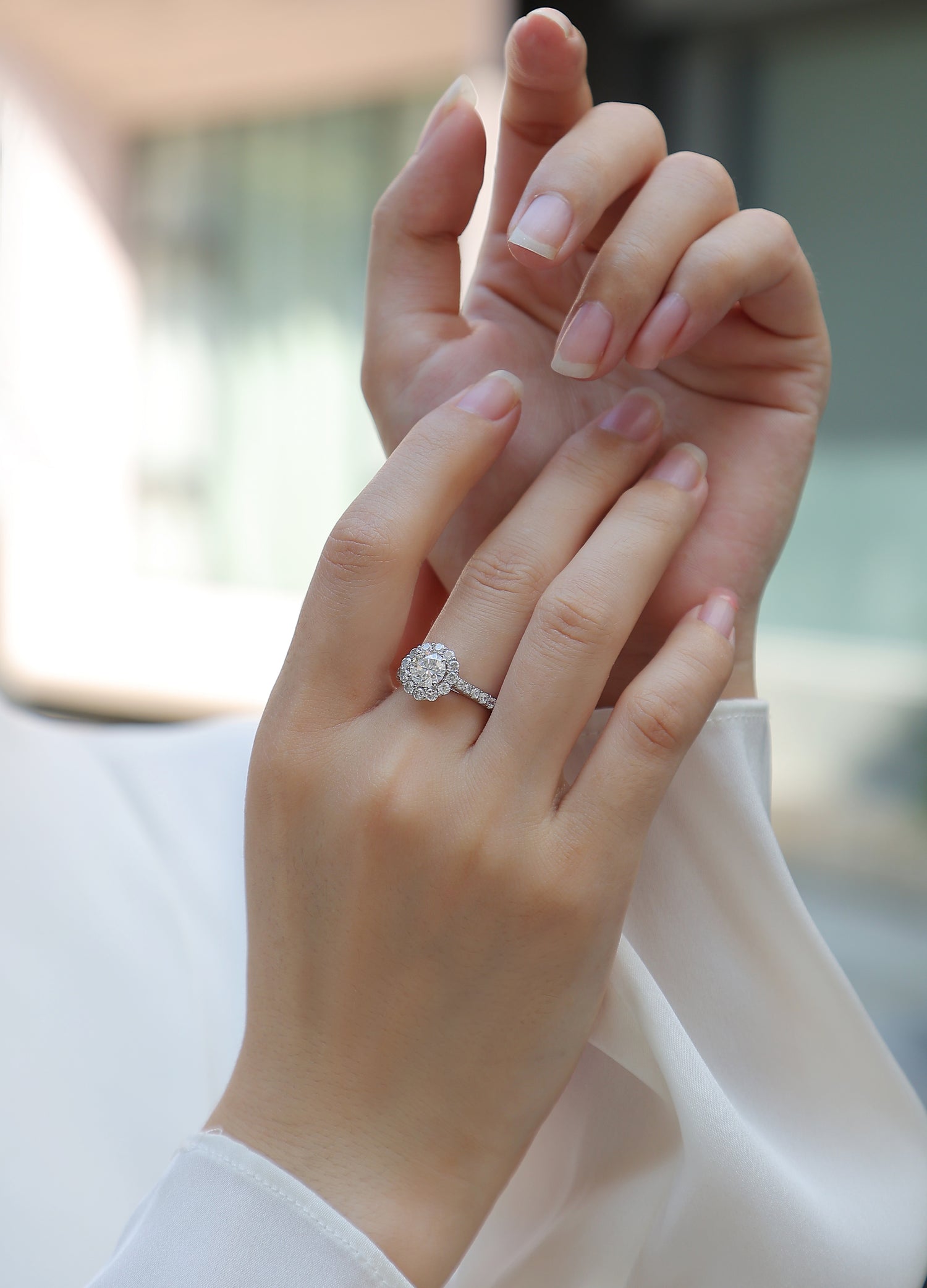 CARISSIE round moissanite halo engagement ring on hand, showing elegant fit and pavé band against white fabric