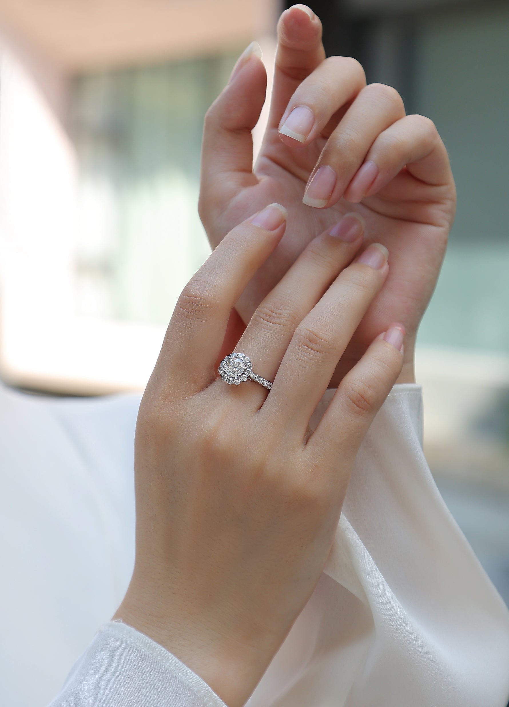 CARISSIE round moissanite halo engagement ring on hand, showing elegant fit and pavé band against white fabric