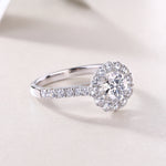 CARISSIE round moissanite halo engagement ring, close-up resting on soft surface, focusing on polished metal and gem clarity