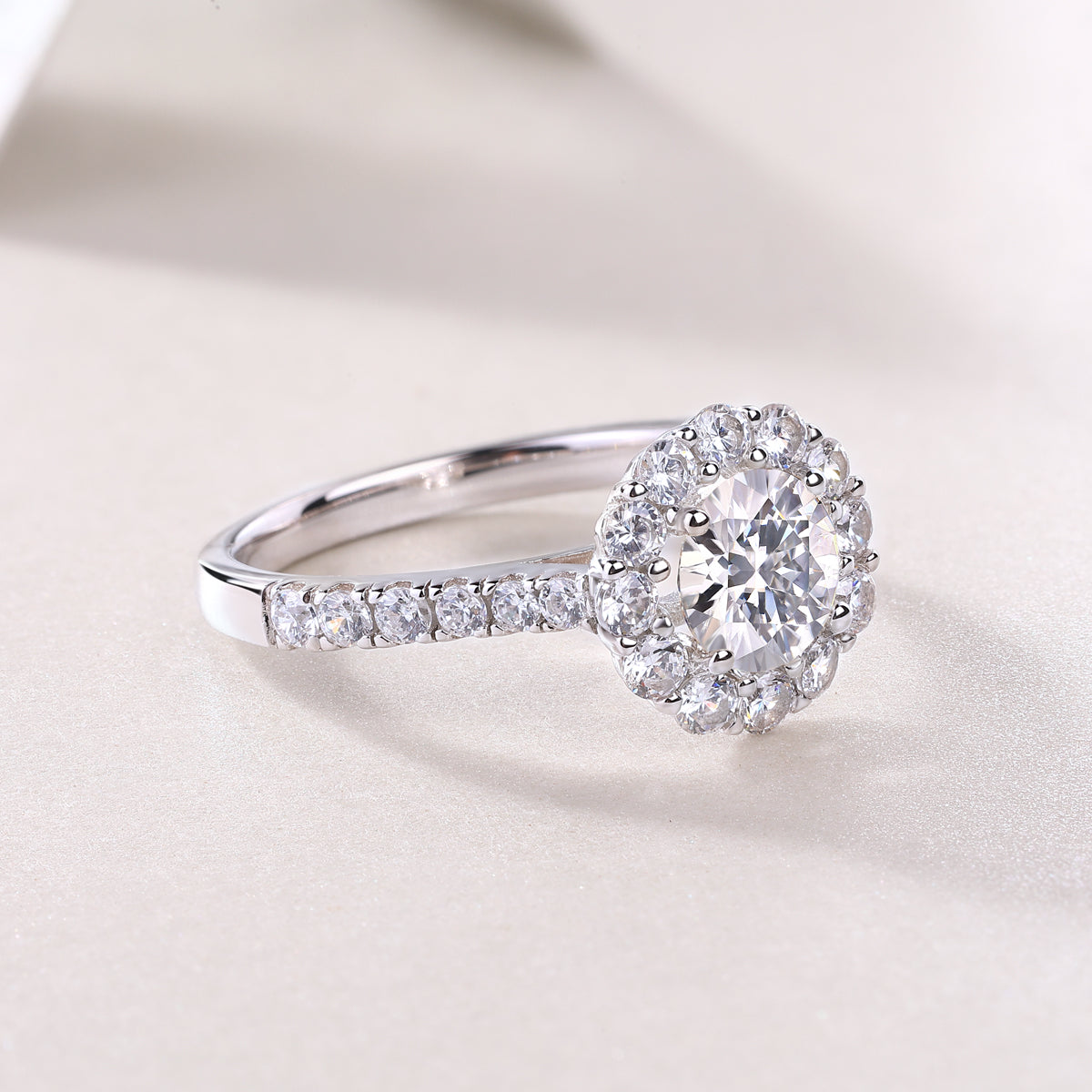 CARISSIE round moissanite halo engagement ring, close-up resting on soft surface, focusing on polished metal and gem clarity