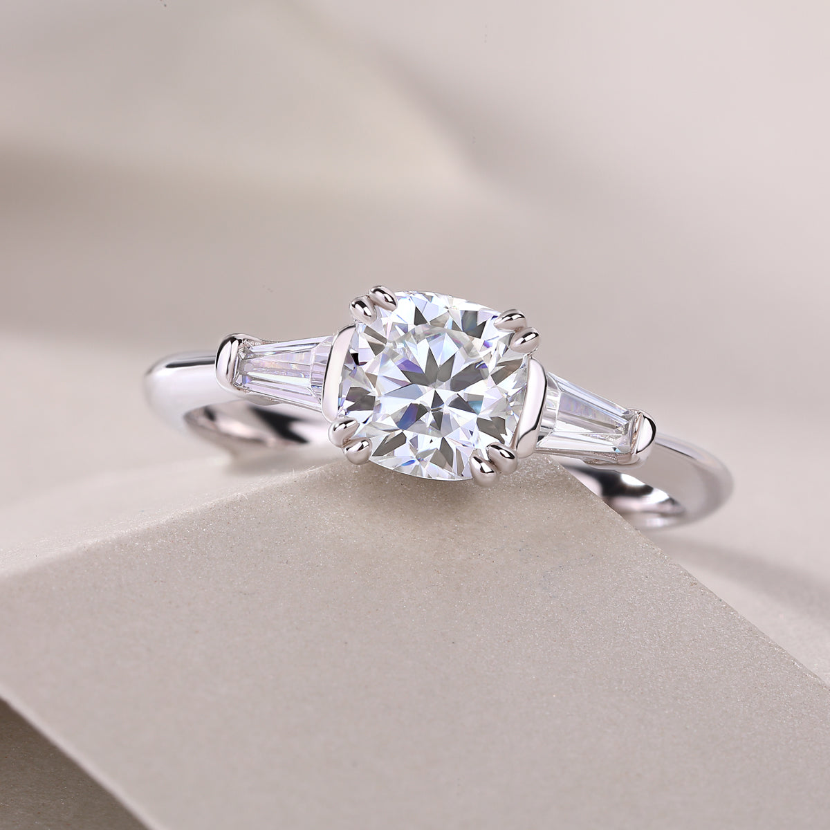 CARISSIE cushion solitaire engagement ring, lifestyle shot on a textured surface emphasizing the brilliance of the moissanite stones