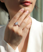 CARISSIE pear moissanite halo ring on model, hand touching chin showing elegant white metal band and brilliant sparkle