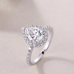 CARISSIE pear moissanite halo ring, three-quarter perspective shot on neutral background focusing on the brilliance of the main stone