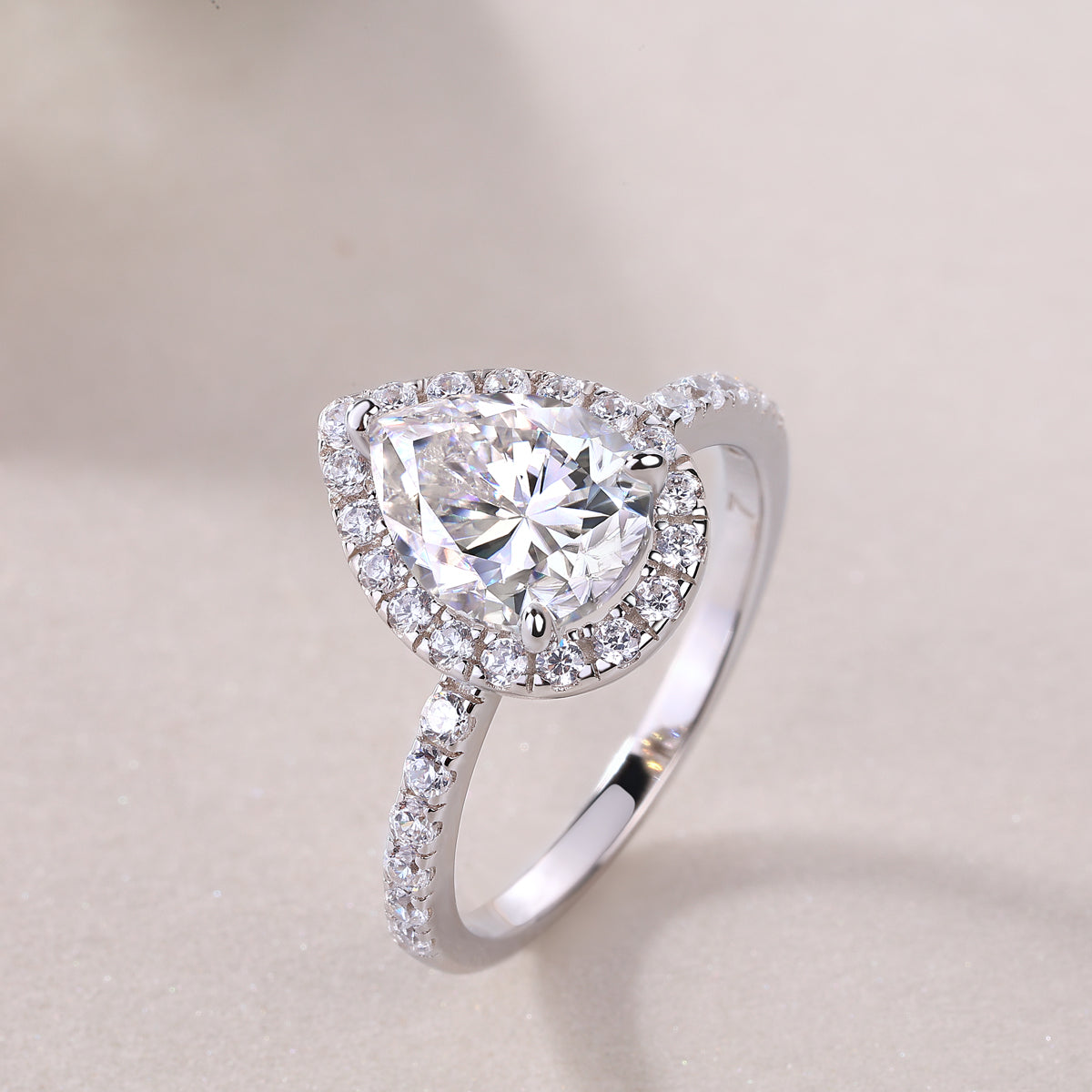 CARISSIE pear moissanite halo ring, three-quarter perspective shot on neutral background focusing on the brilliance of the main stone