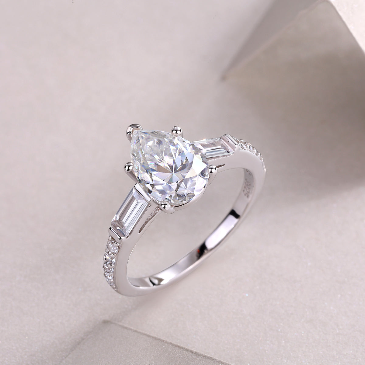 CARISSIE pear moissanite ring angled studio shot, capturing light reflection on the facets and polished silver finish