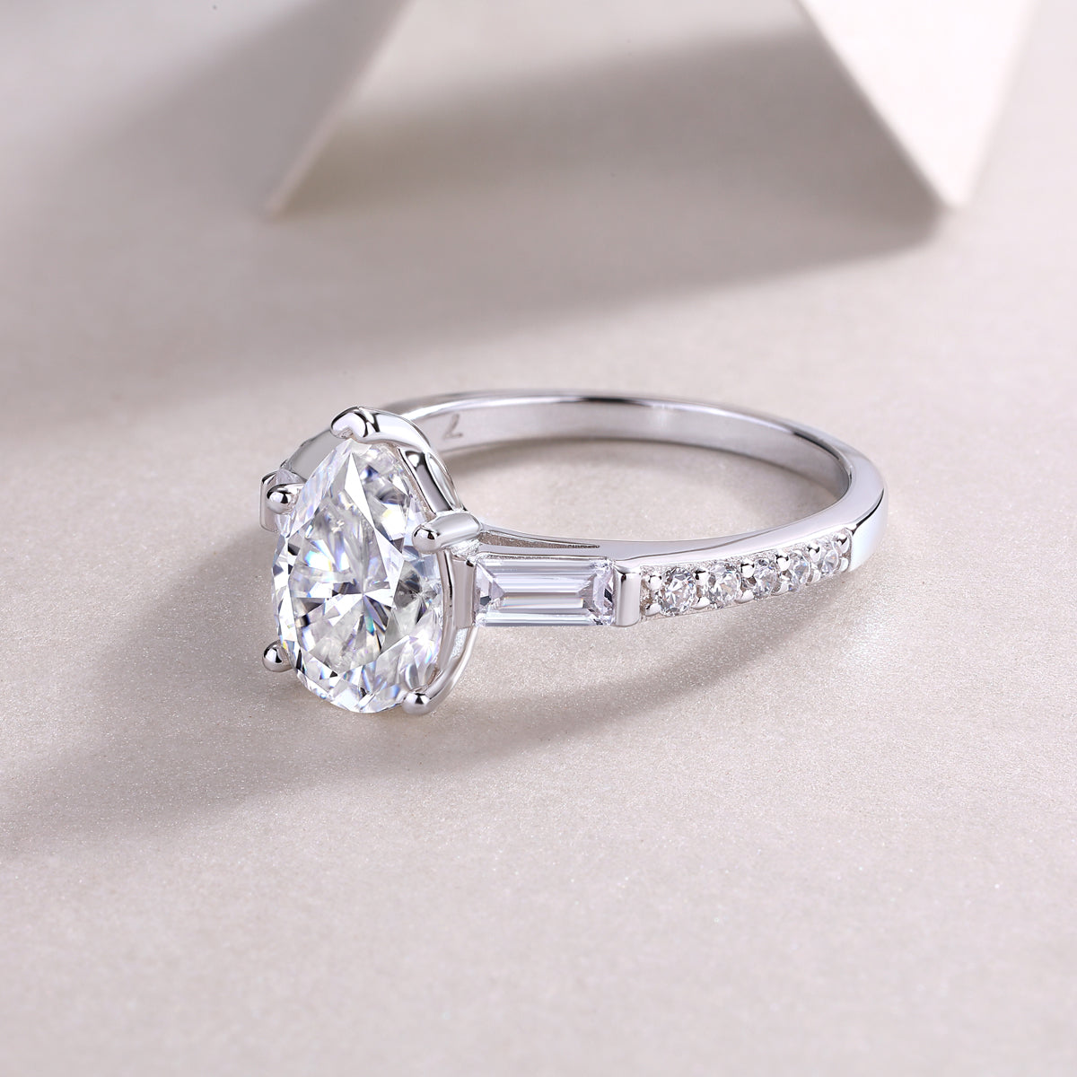 CARISSIE pear moissanite ring resting on surface, emphasizing the elongated silhouette and detailed shoulder pave work