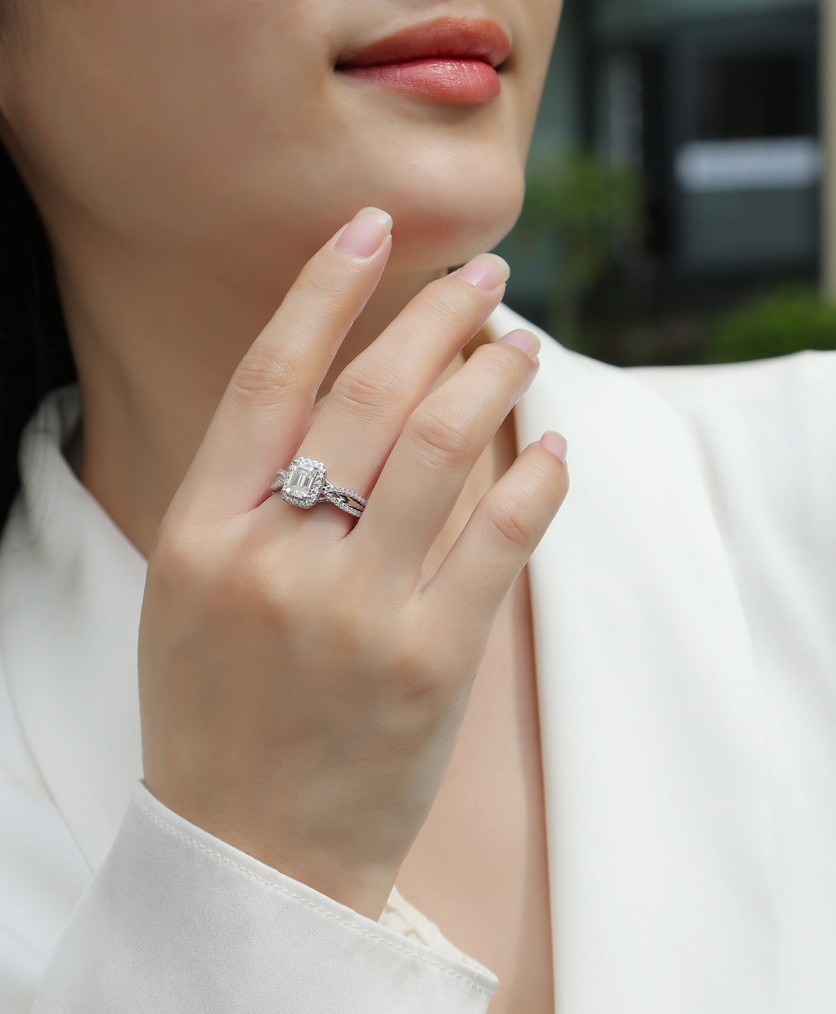 CARISSIE emerald cut moissanite halo ring worn on finger, front view highlighting the dense stone halo and criss-cross design