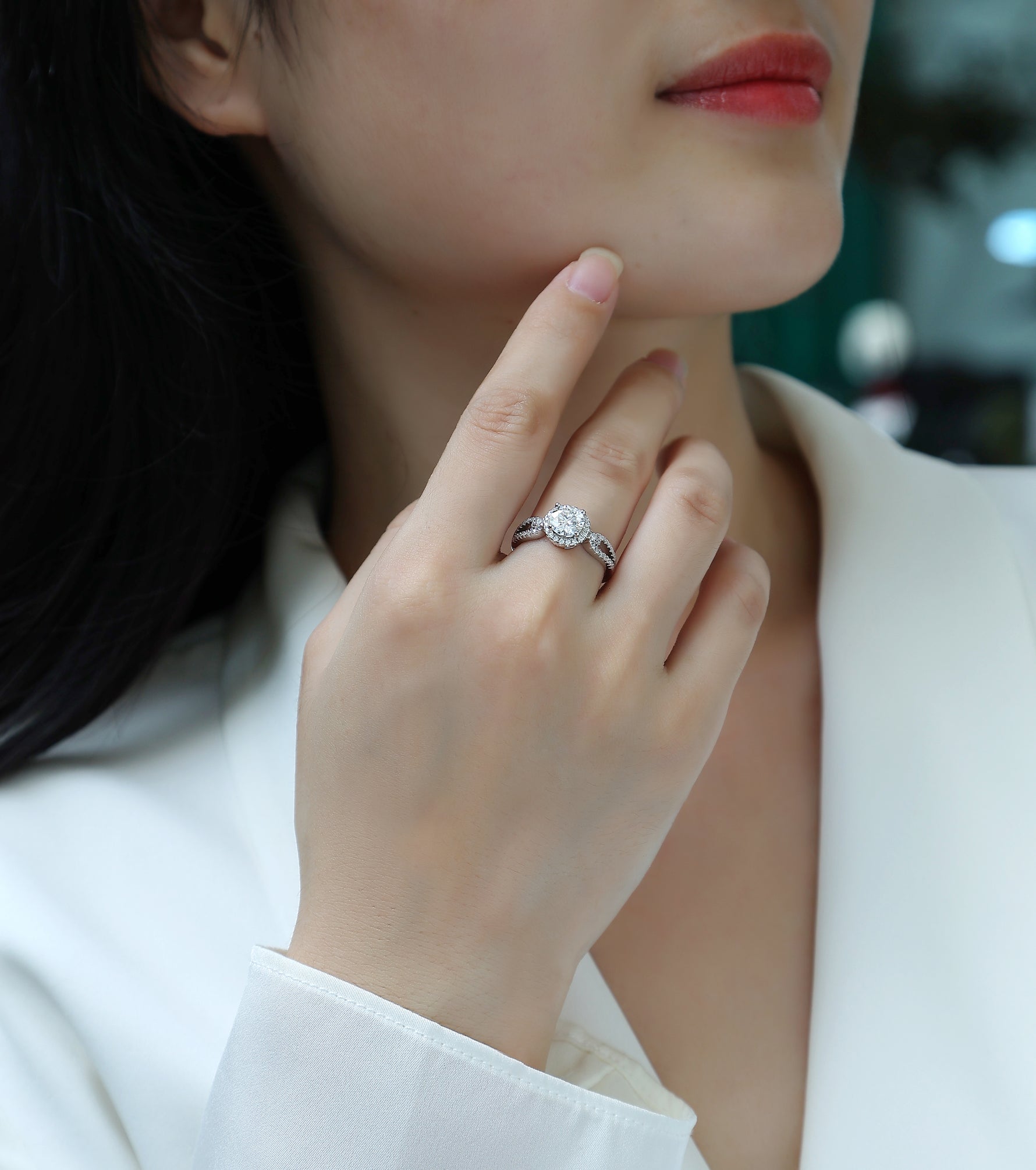 CARISSIE round moissanite halo ring on model, close-up of hand touching chin highlighting silver-tone metal and sparkle