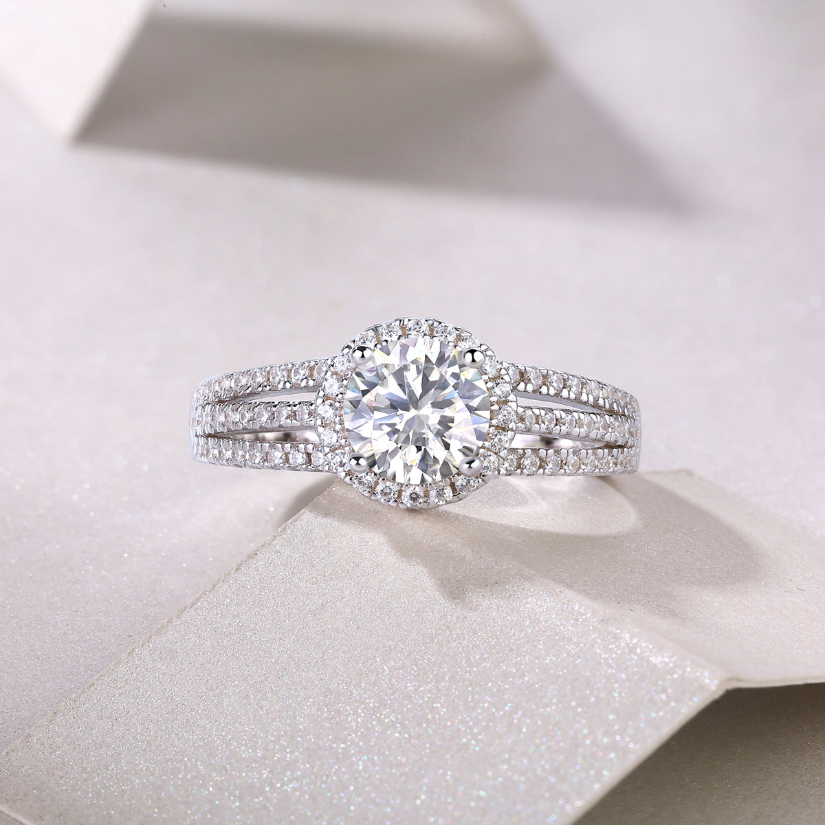 CARISSIE round moissanite halo ring on glittery fabric, straight-on view emphasizing sparkle and brilliance