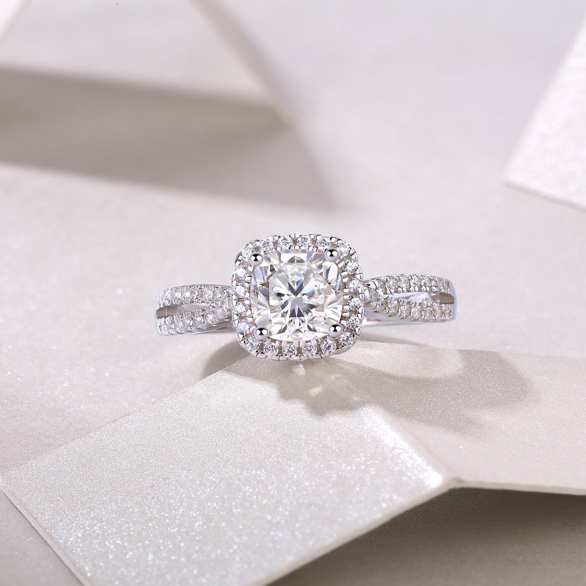 CARISSIE cushion moissanite halo engagement ring on white textured surface, top-down perspective emphasizing geometric shape