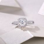 CARISSIE cushion moissanite halo engagement ring on white textured surface, top-down perspective emphasizing geometric shape