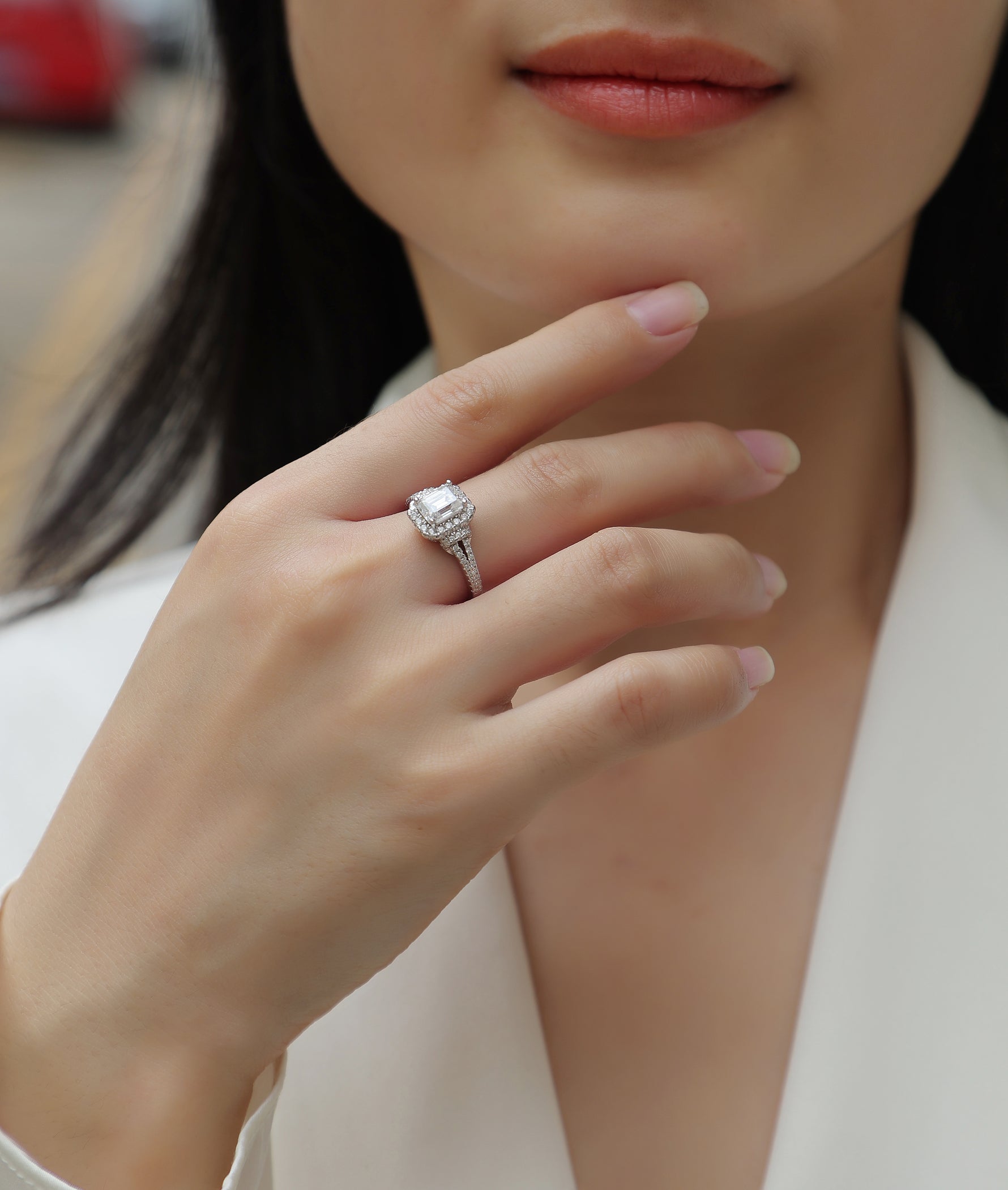 CARISSIE emerald cut moissanite halo ring on hand, close-up view near face highlighting sparkle