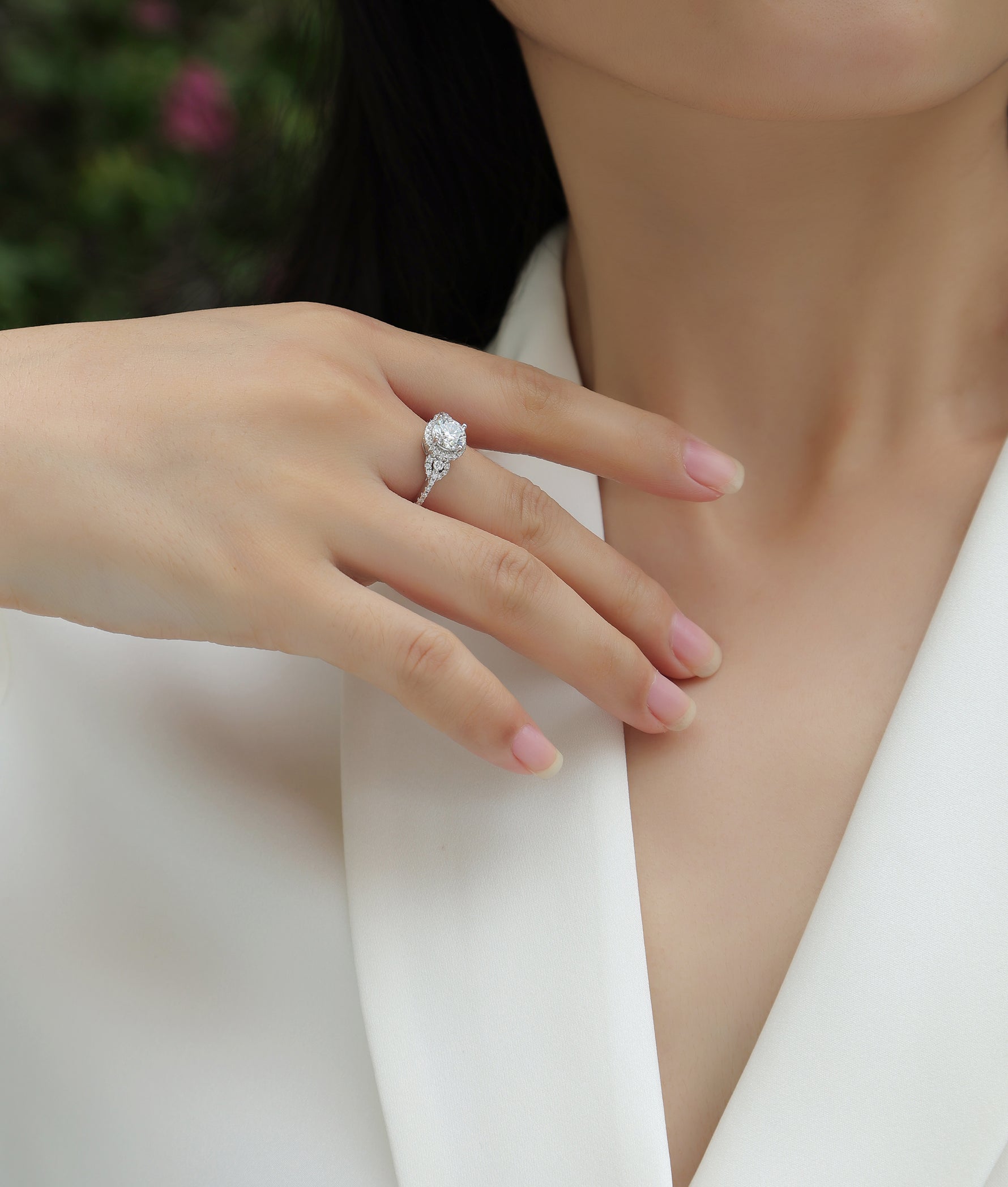 CARISSIE round moissanite halo ring on model's hand resting on collarbone, highlighting the elegant profile and brilliant cut