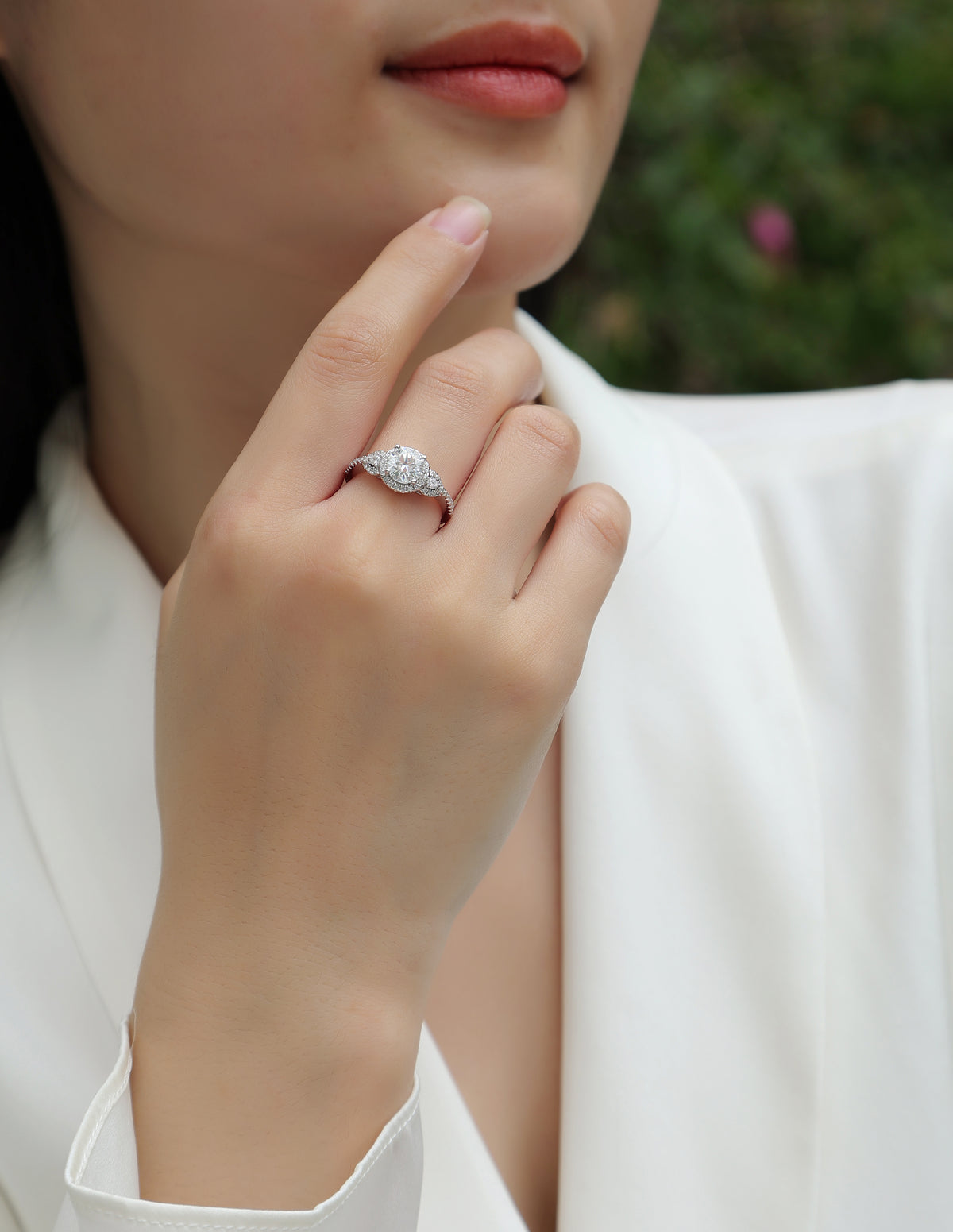 CARISSIE round moissanite halo ring on model's hand near face, showing vintage-inspired pavé shoulders and sparkling center stone