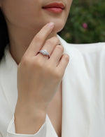 CARISSIE round moissanite halo ring on model's hand near face, showing vintage-inspired pavé shoulders and sparkling center stone