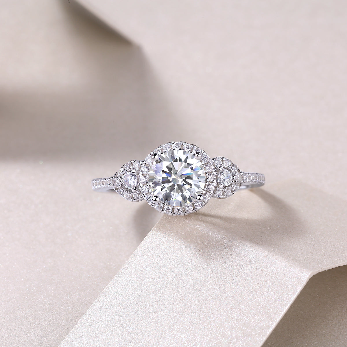 CARISSIE round moissanite halo ring resting on textured paper, close-up shot emphasizing the brilliance of the central gemstone