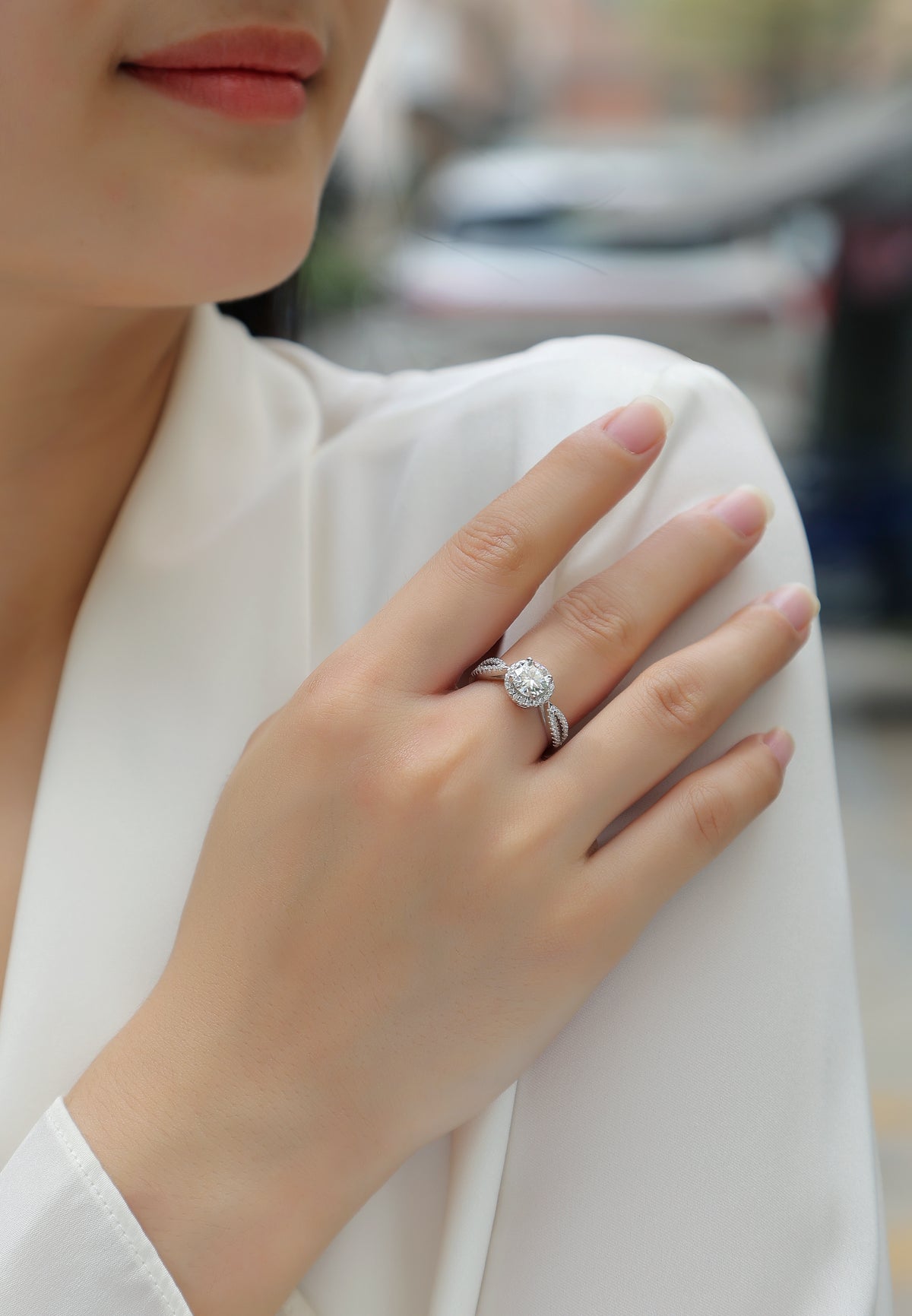 CARISSIE round moissanite halo ring, lifestyle shot on model showing twisted pavé band against white fabric