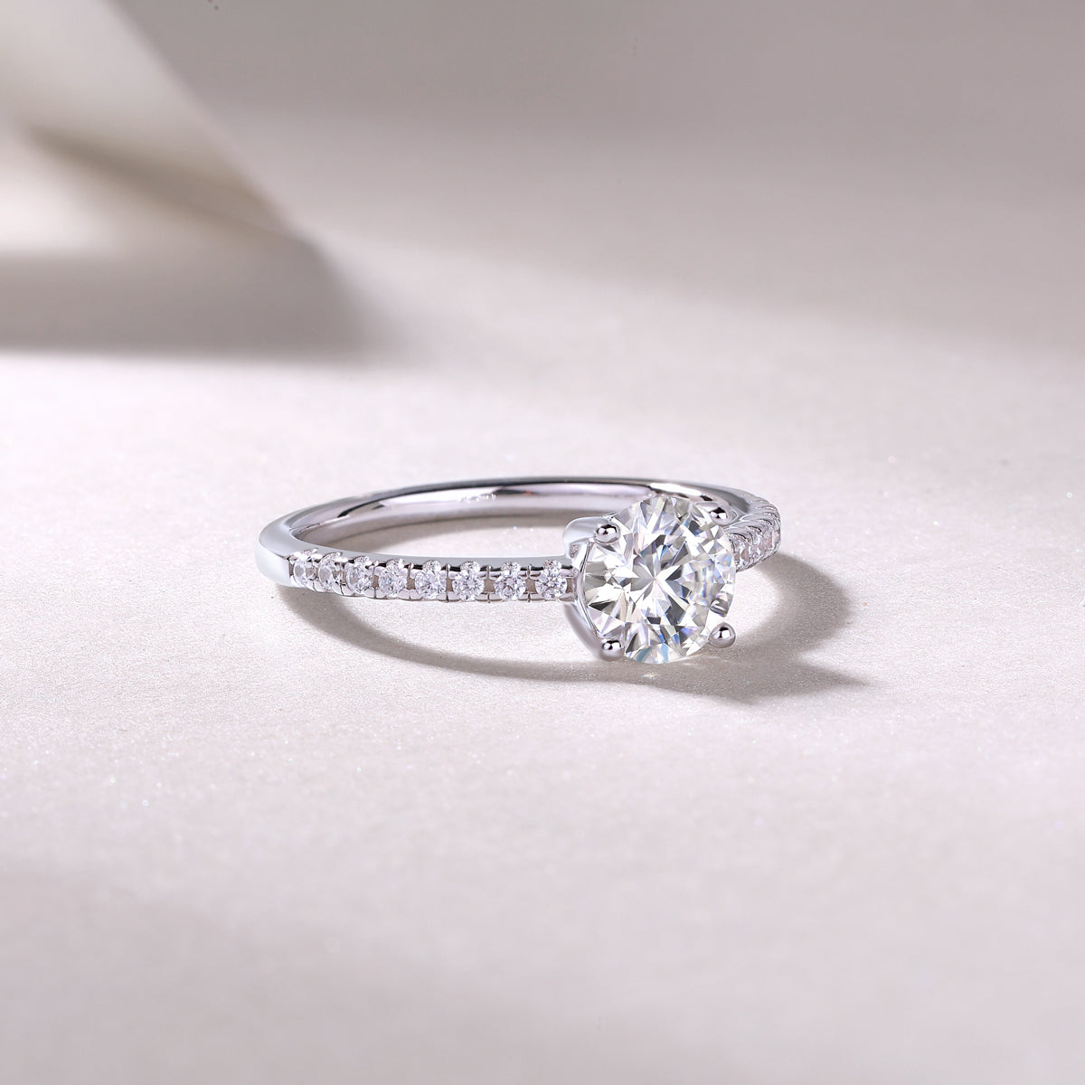 CARISSIE round moissanite solitaire ring lifestyle shot, resting on textured surface with soft shadows accentuating the fire