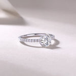 CARISSIE round moissanite solitaire ring lifestyle shot, resting on textured surface with soft shadows accentuating the fire