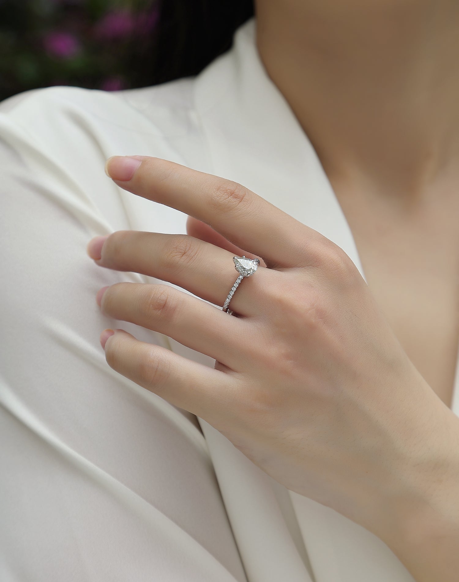 CARISSIE pear moissanite engagement ring on model, hand resting on white fabric displaying side profile sparkle