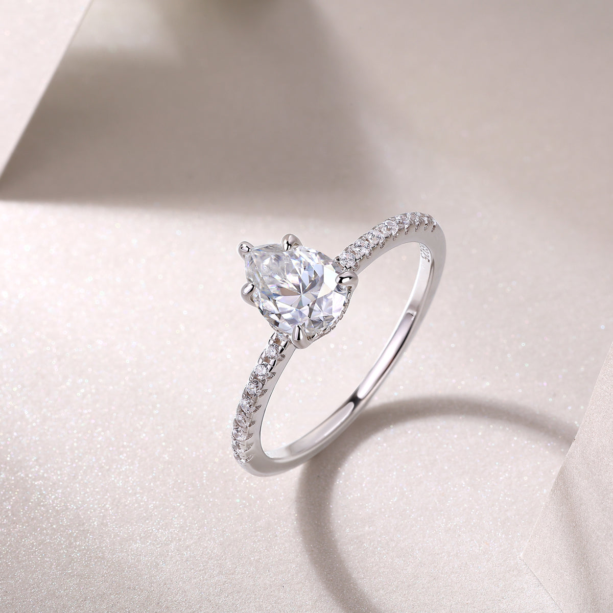CARISSIE pear moissanite solitaire ring angled shot on textured surface, catching light on silver metal